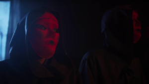 Cloaked woman in semi-darkness wearing sinister mask