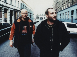 Pusher Image - two younger men, one a skinhead walking down the centre of a road