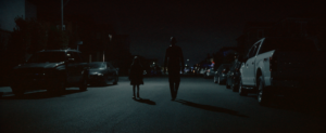 An adult and a child walking down middle of the road at night